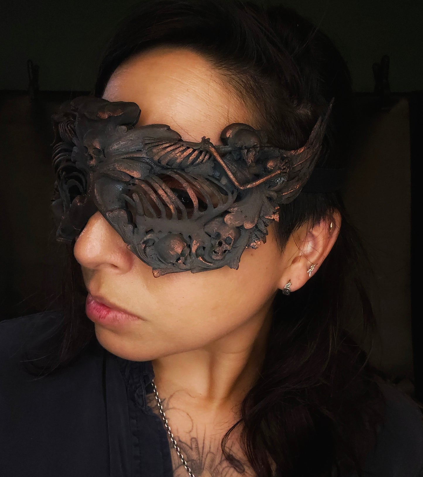 A costume mask decorated in skeletons, skulls, wings, and filigree. Human ribcages cover the eyes for a false blind effect