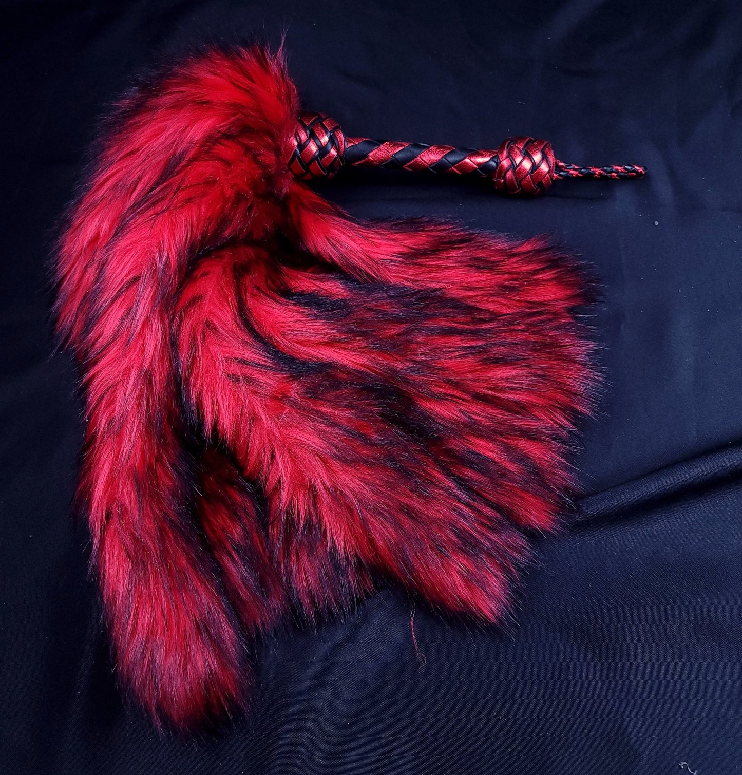 A red fluffinator flogger with weighted faux fur tails for impact play