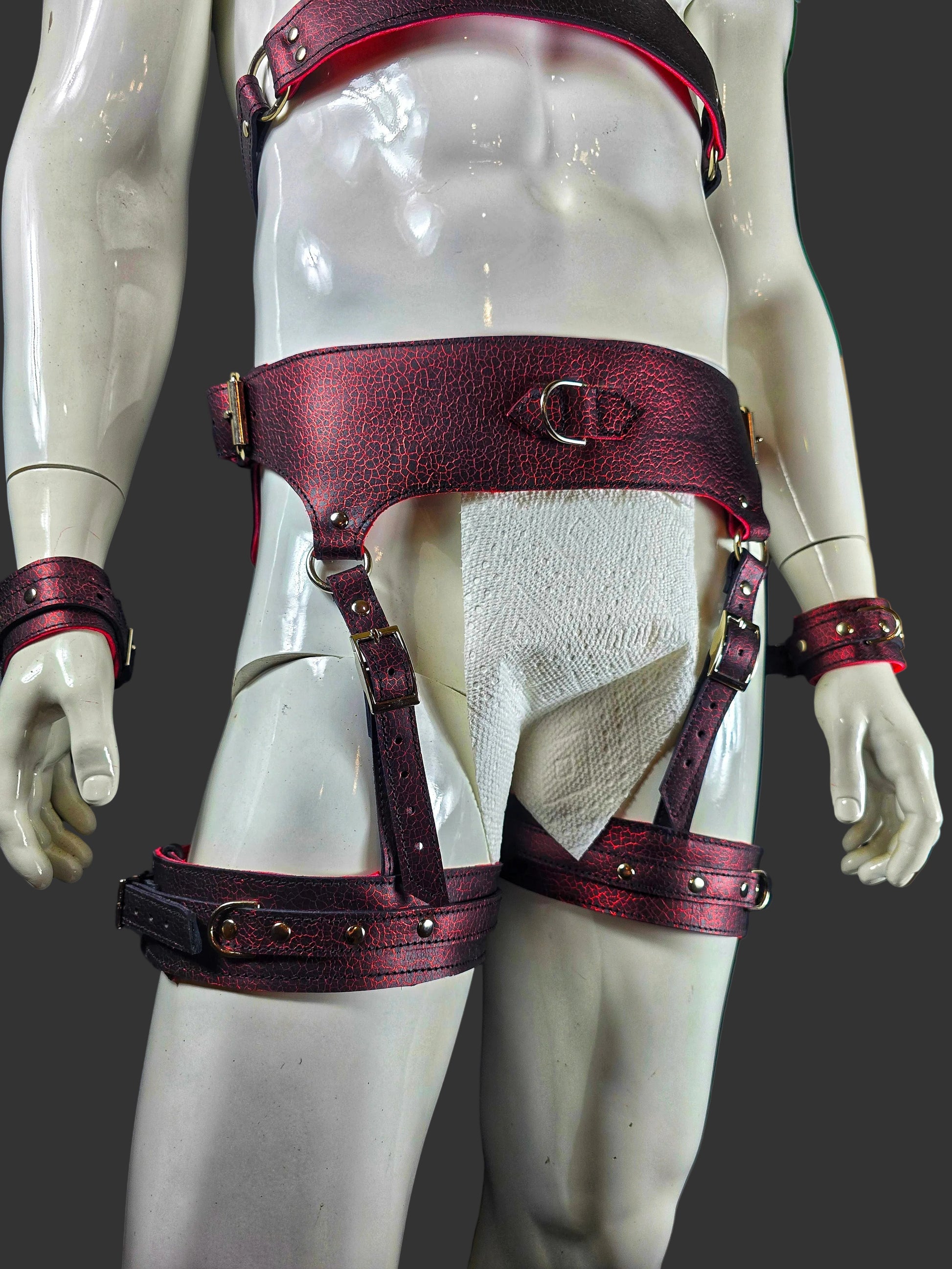 Mannequin wearing a red leather harness with silver accents against a dark background